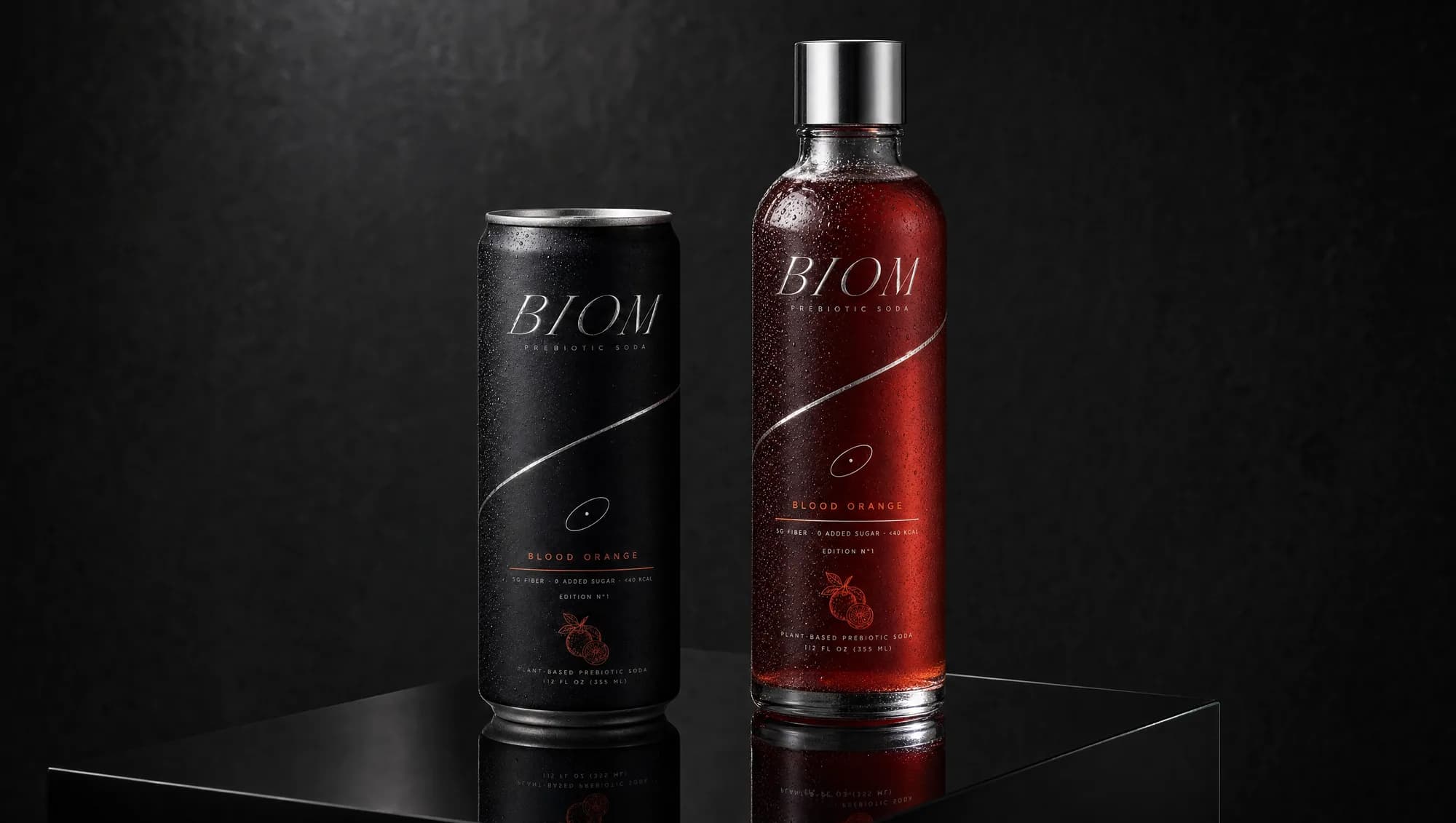 The BIOM can and bottle, Blood Orange, chrome and charcoal against a dark surface.